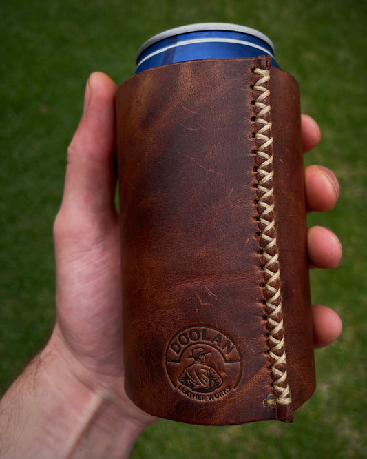 Brown leather can cooler with braided handle held by a hand against a green background