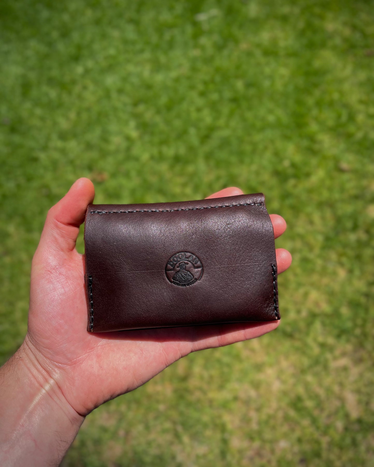 Brown leather fishing lure case held in a hand against a grassy background