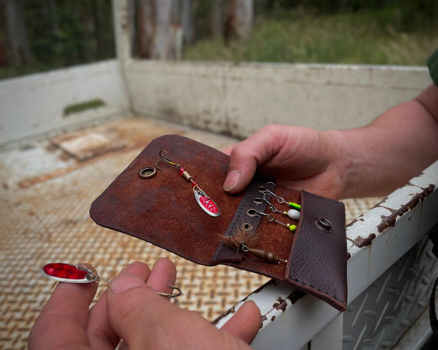Brown leather case with fishing lures held by a person against a rustic background