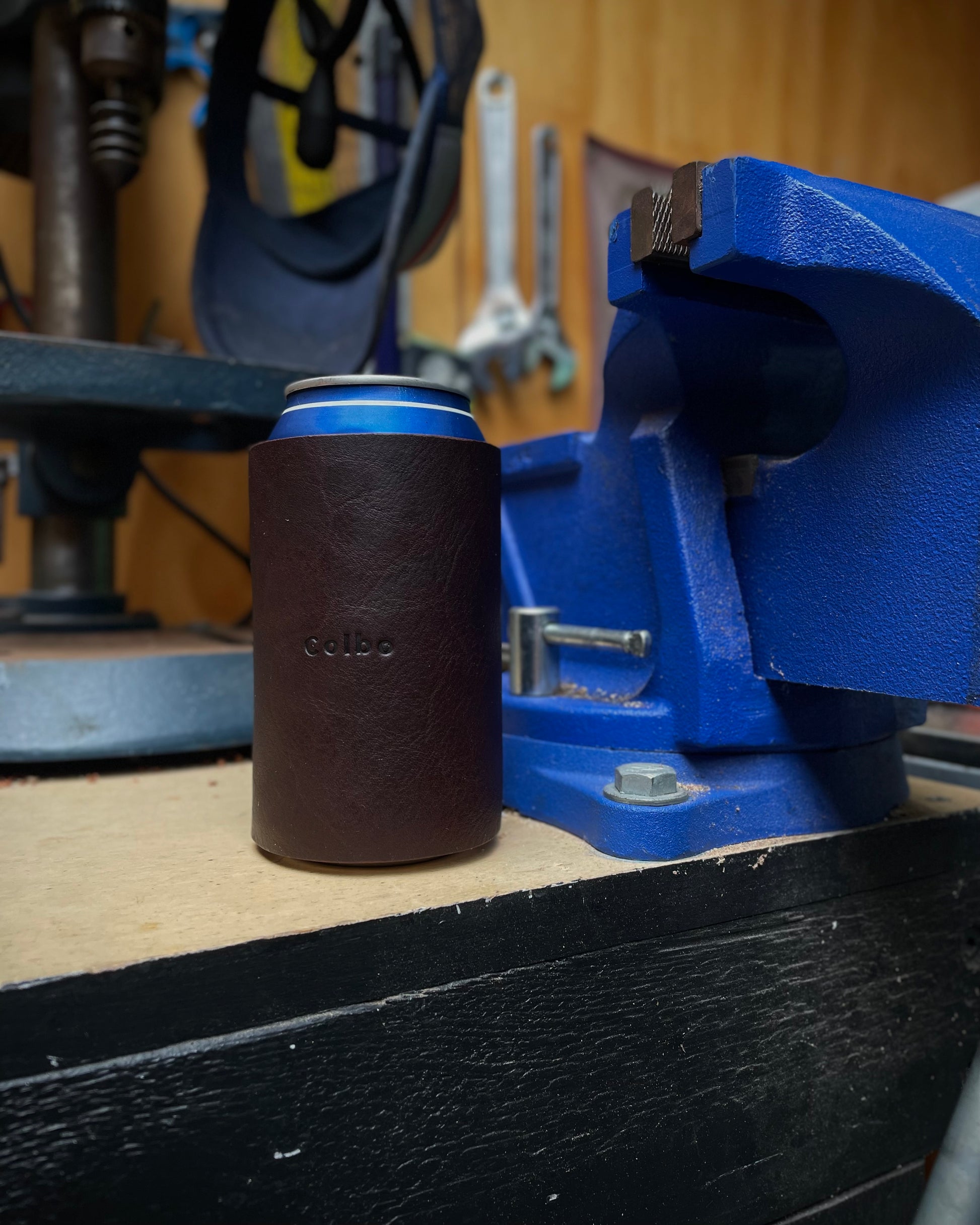 Can with a brown leather sleeve on a blue vise in a workshop setting