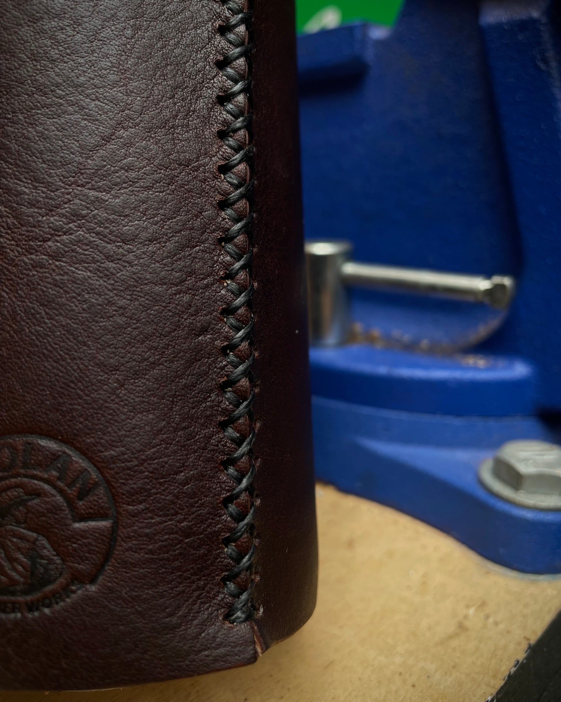 Close-up of a brown leather can holder with stitching detail, blurred blue tool in the background.