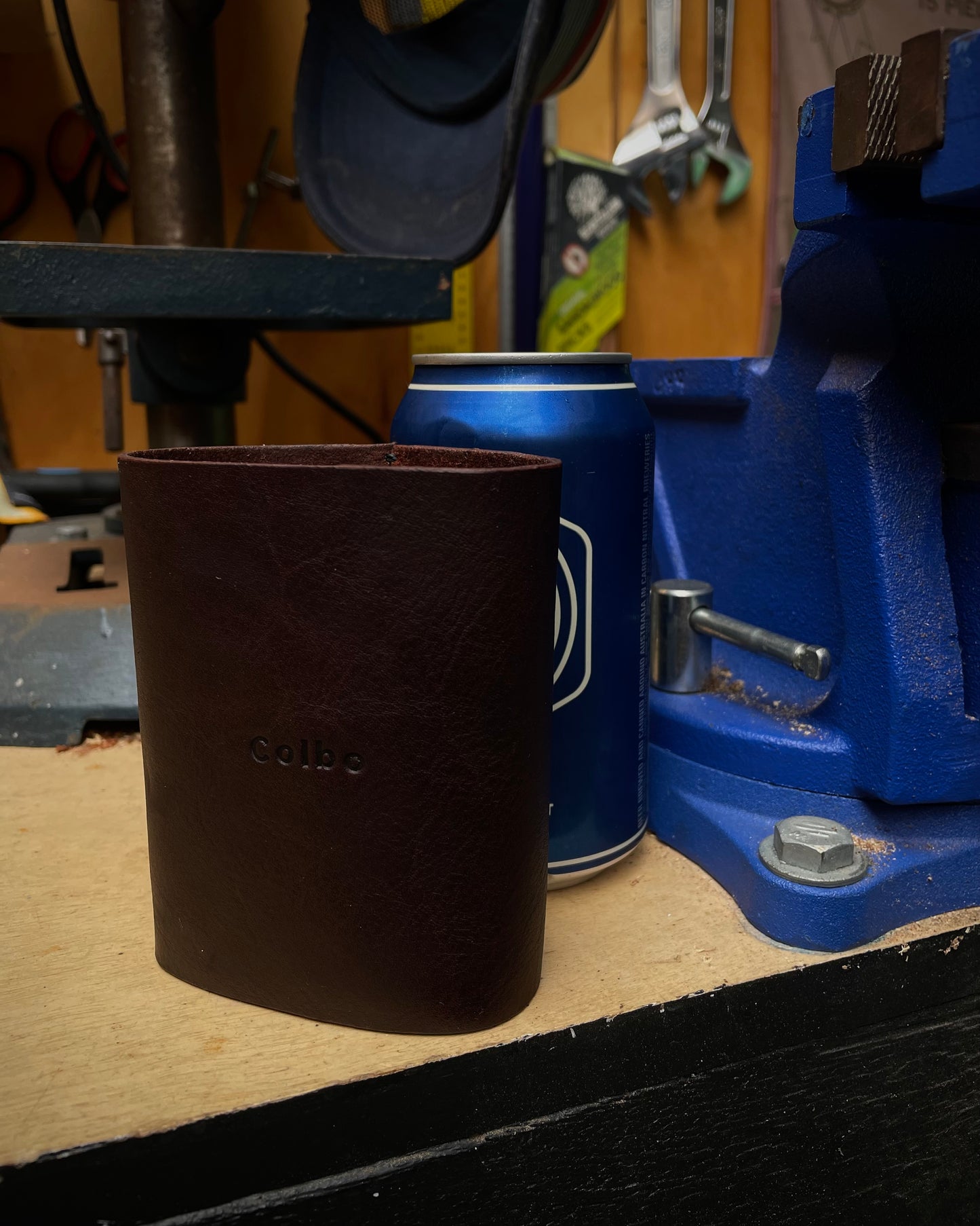 Brown leather cup holder on a workbench with tools in the background