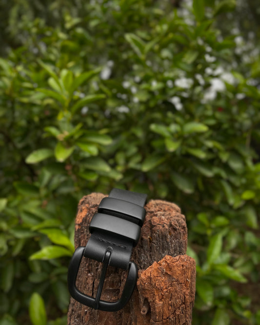 Black leather belt on a wooden post with green foliage in the background