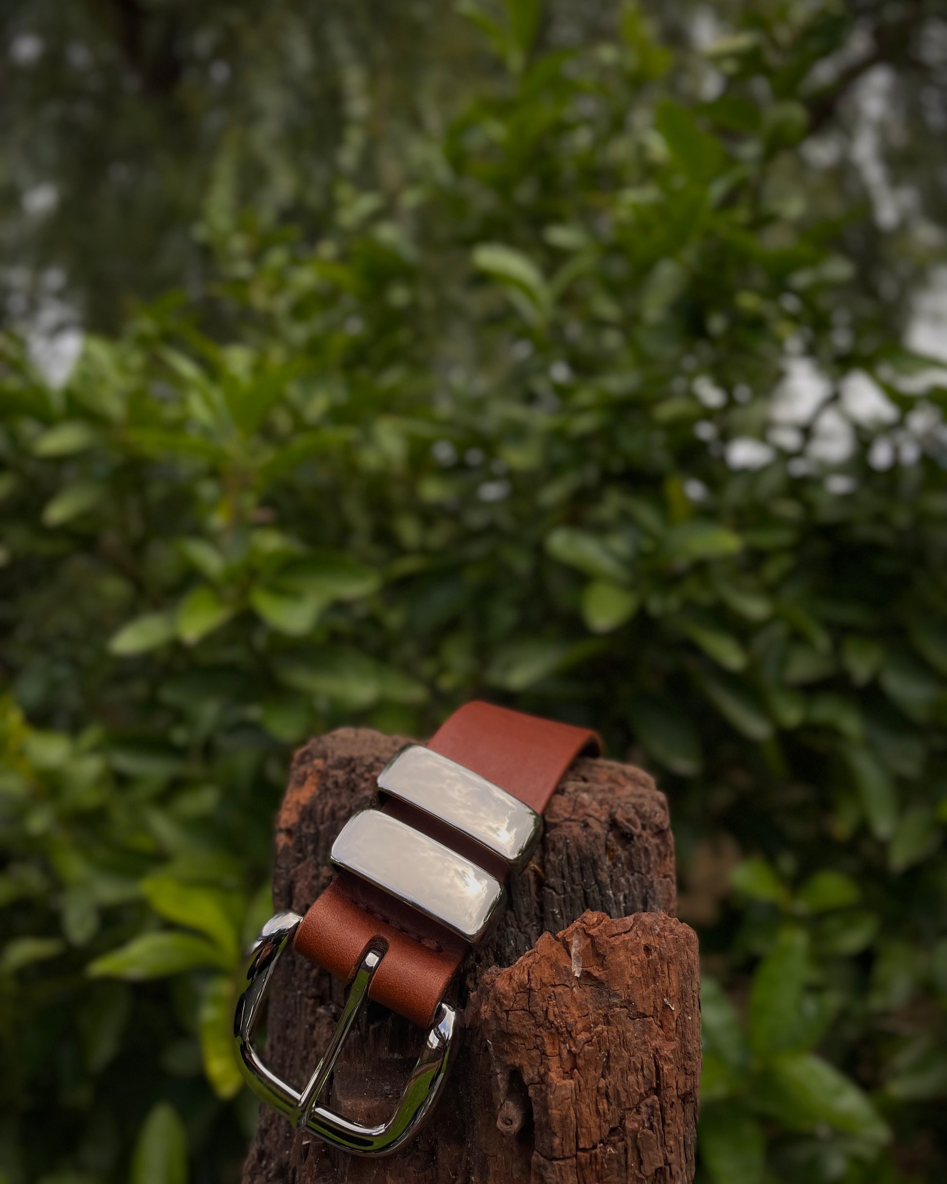 Brown and white leather belt on a wooden post with a blurred green foliage background