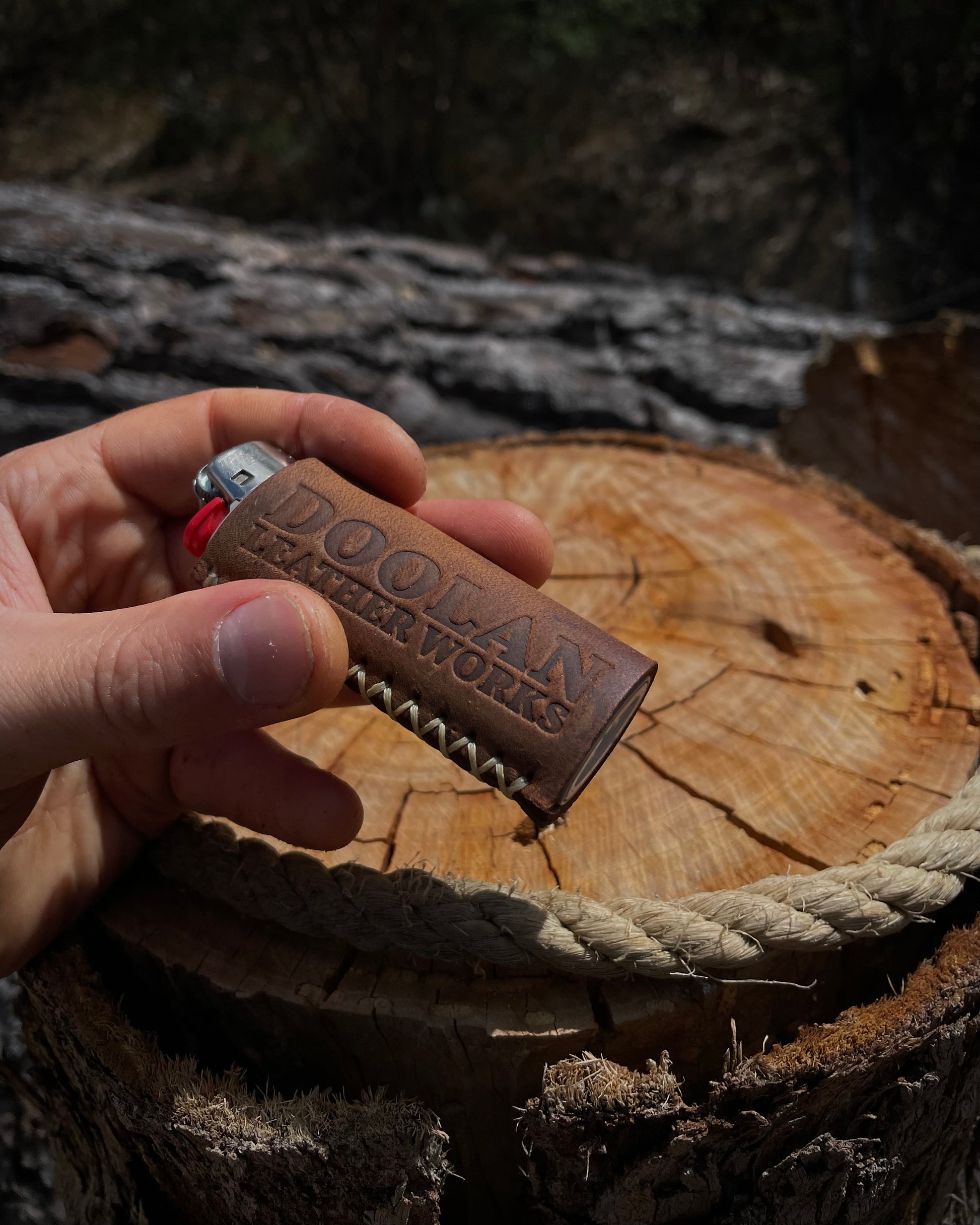 Hand holding a leather lighter case with 'Doohan Leather Works' branding on a wooden surface.