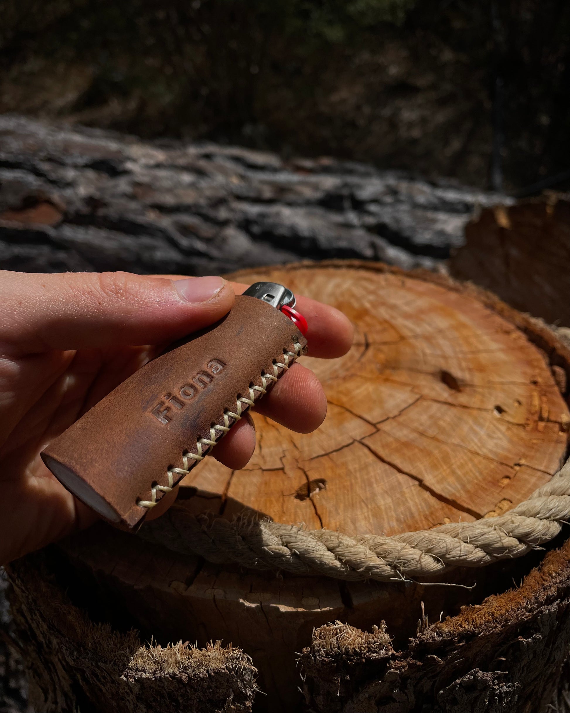 Hand holding a leather lighter with 'Fiona' custom name branding on a wooden surface.