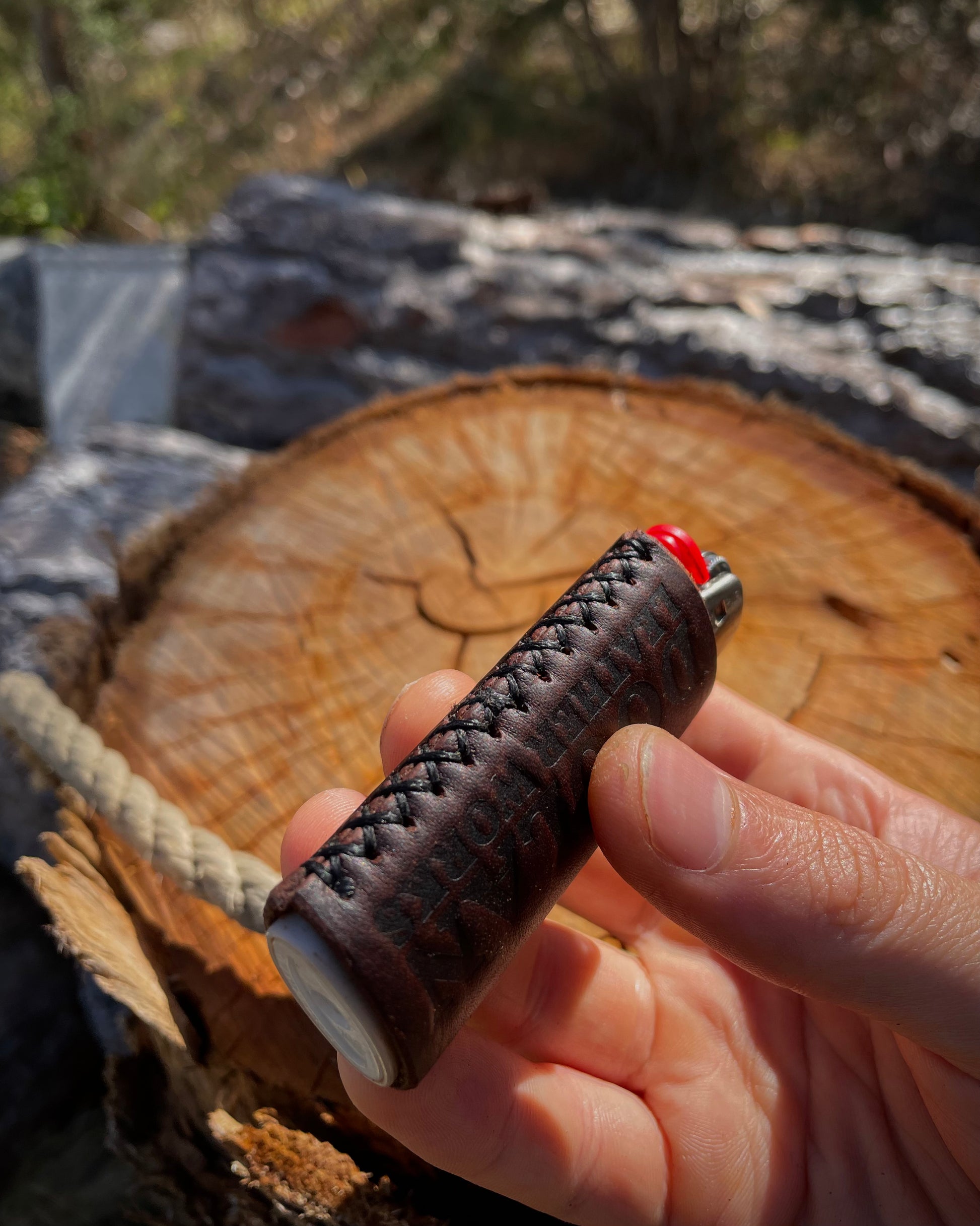 Hand holding a leather-wrapped lighter with a blurred natural background