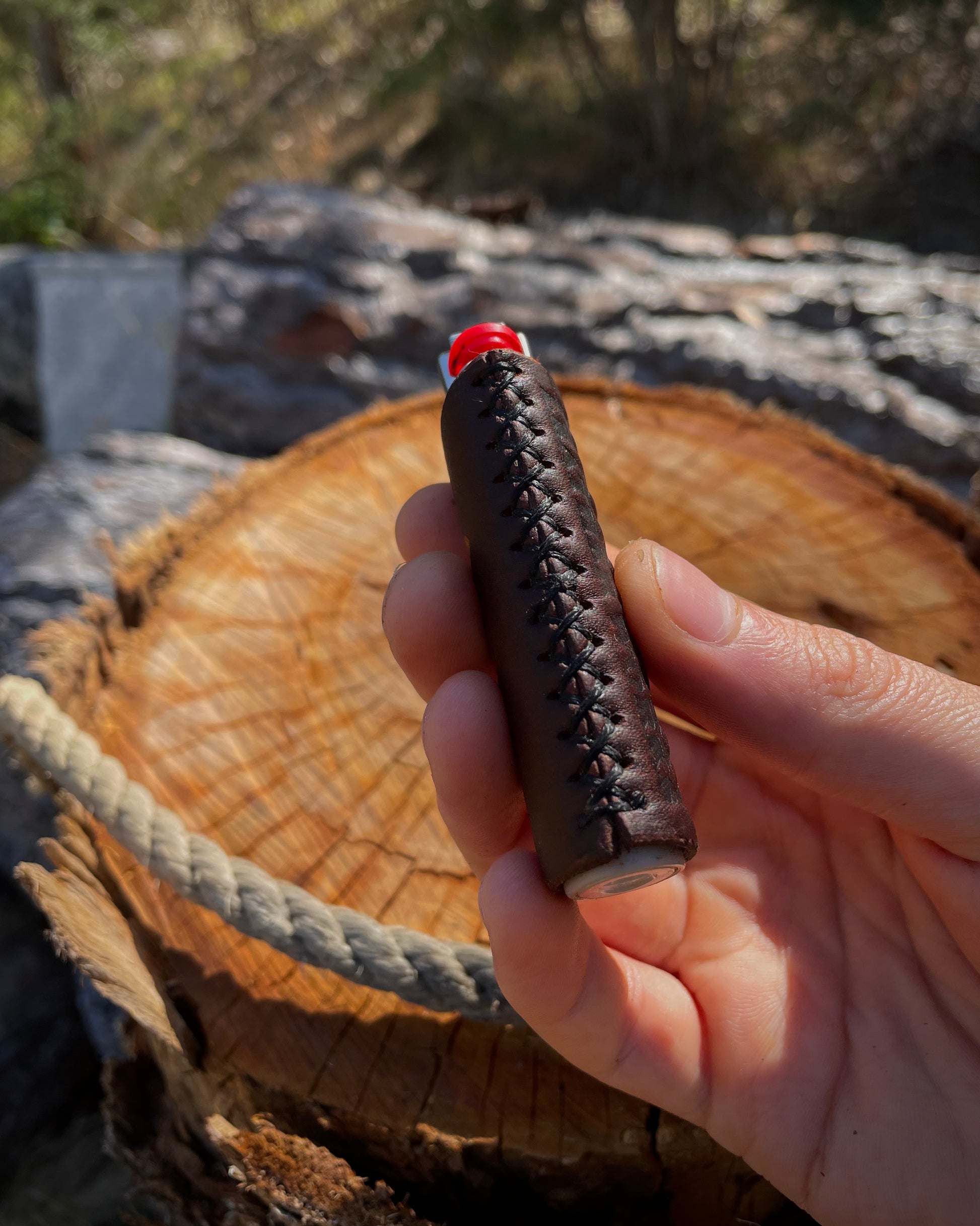 Hand holding a brown leather lighter cover with a red top over a wooden surface