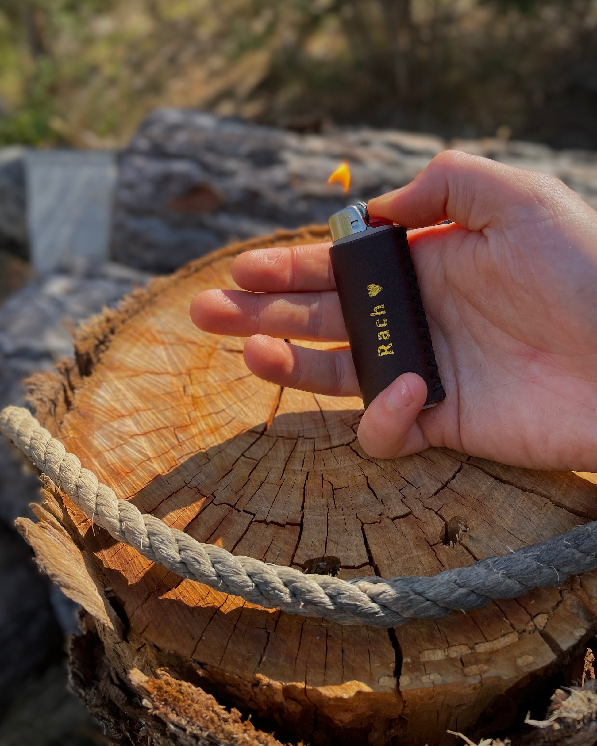 Hand holding a brown leather lighter cover with 'Rach' engraved on it over a wooden surface.
