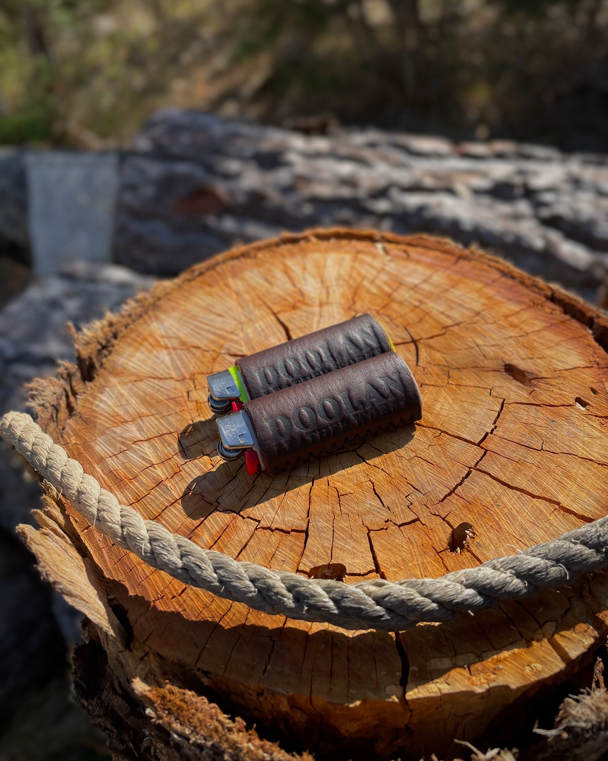 Two leather lighter covers on a wooden log with a rope