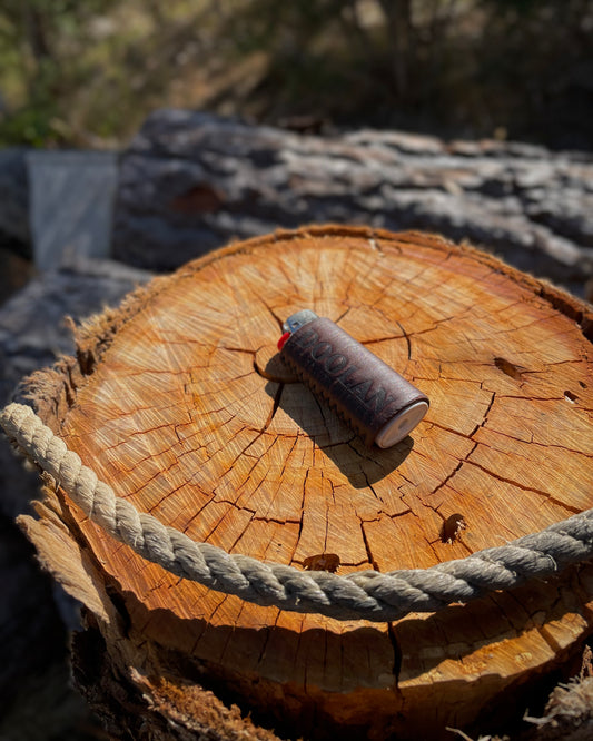 Leather lighter sleeve with rope on a wooden log with a blurred natural background