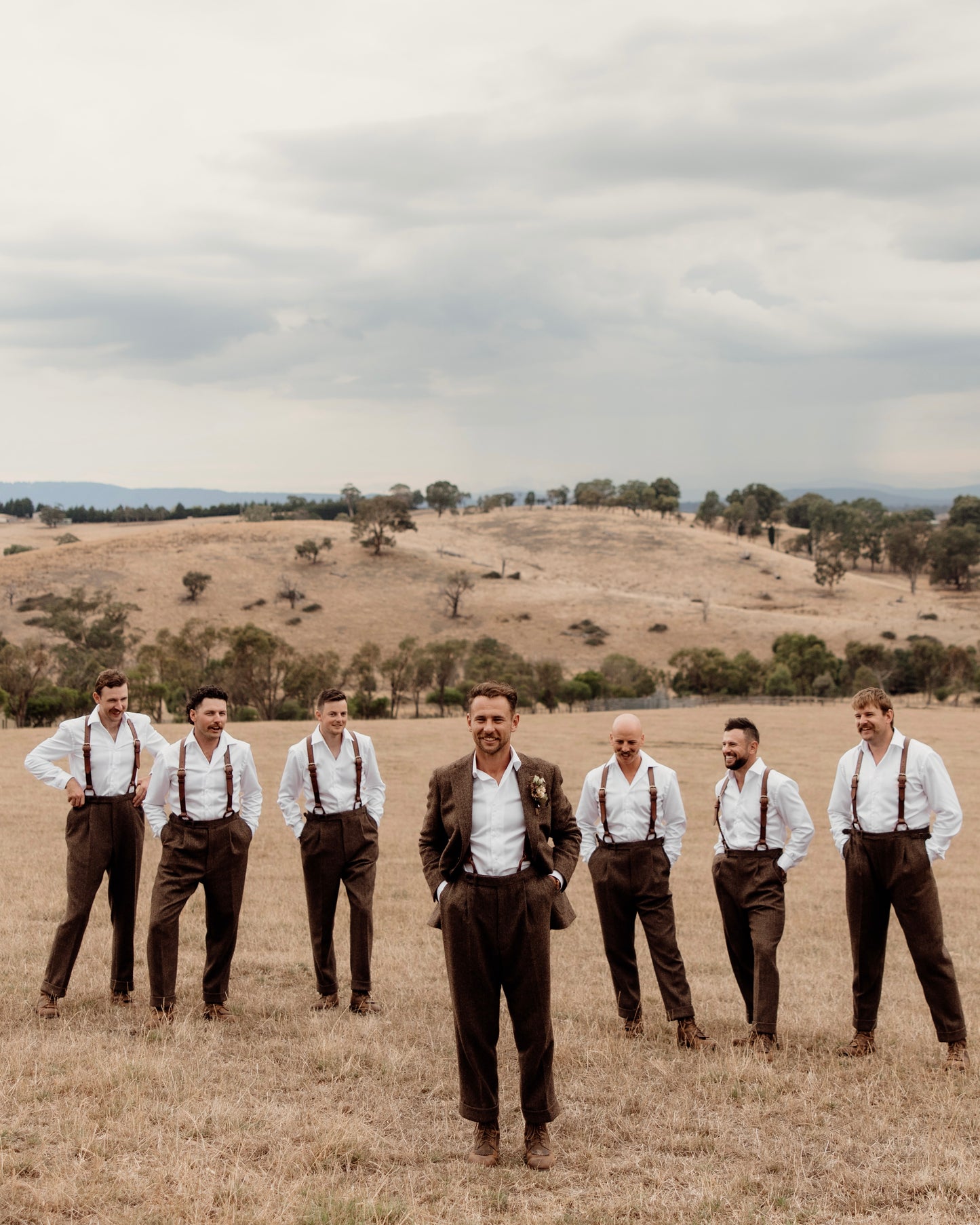 Men in suspenders standing in a field with a scenic background