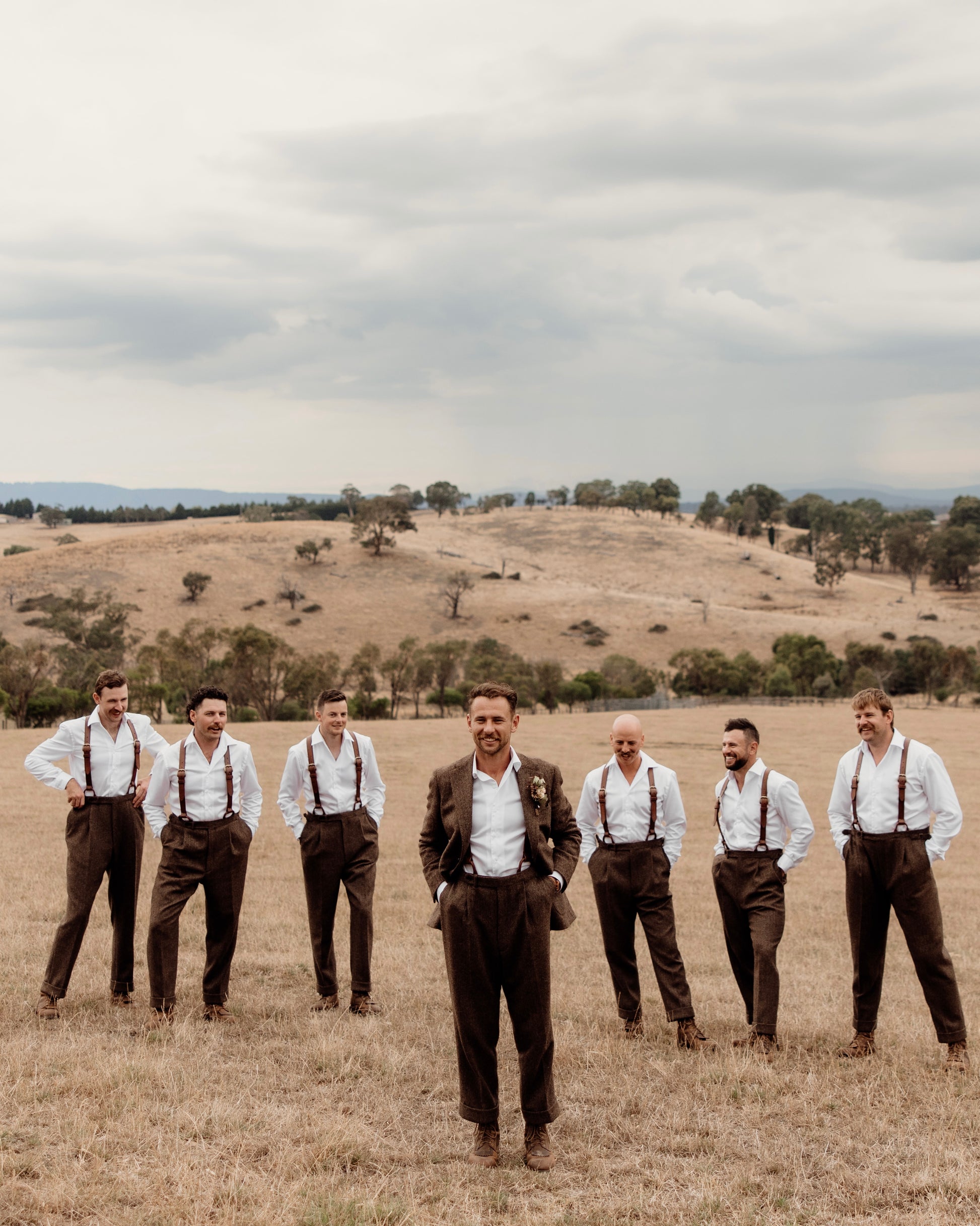 Men in suspenders standing in a field with a scenic background