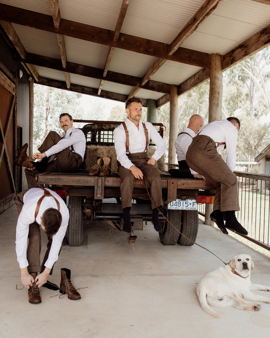 Men in formal attire sitting on a truck with a dog nearby, outdoors.