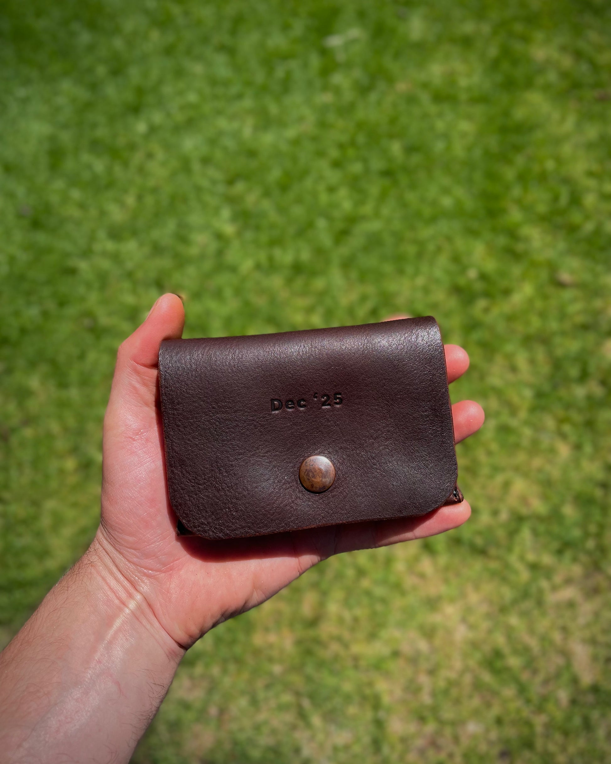 Brown leather fishing lure case held in a hand with a grassy background