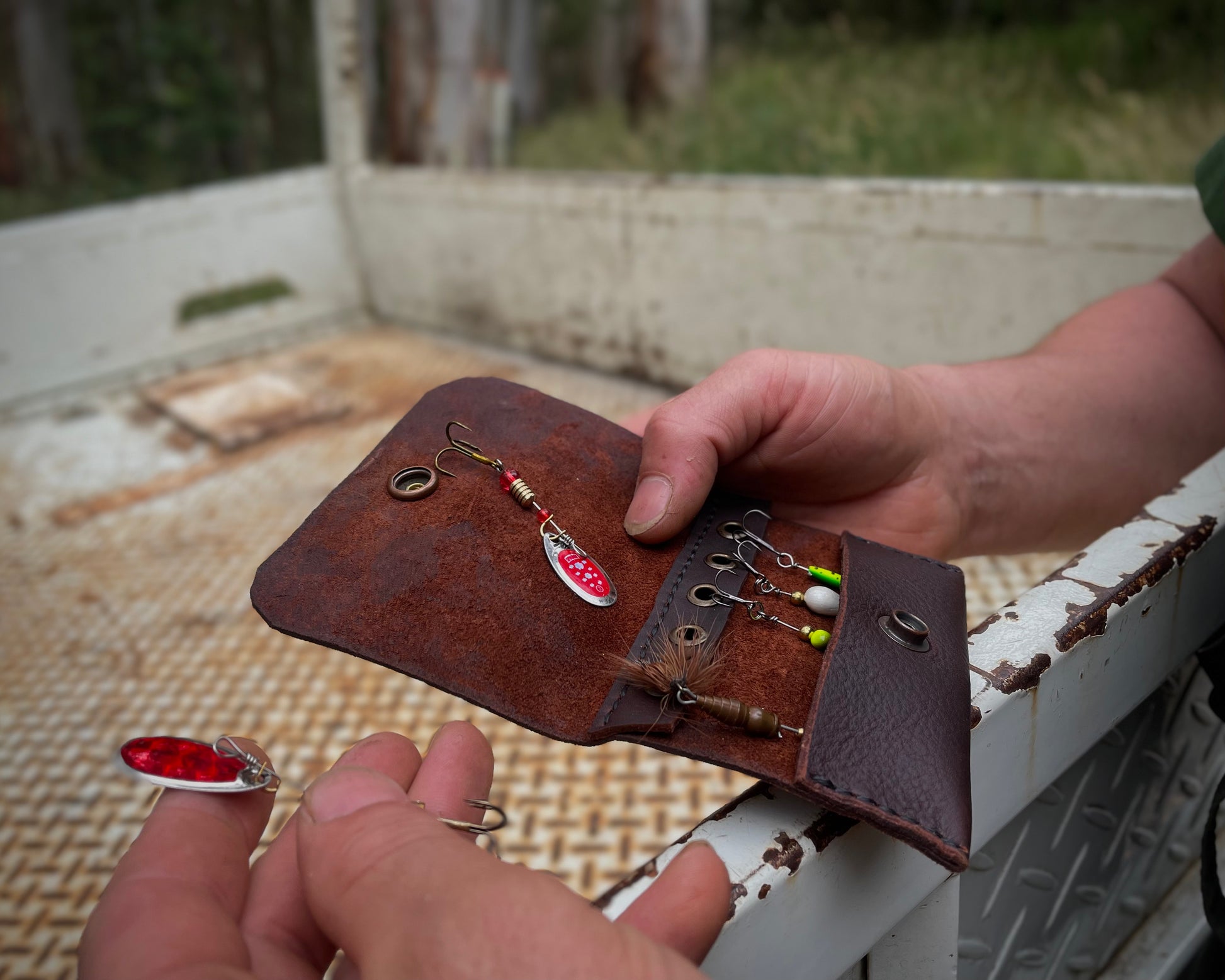 Brown leather case with fishing lures held by a person against a rustic background